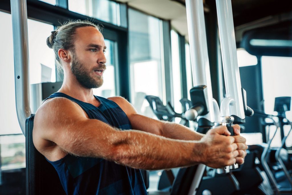Young fit male using pec deck machine in muscle shirt